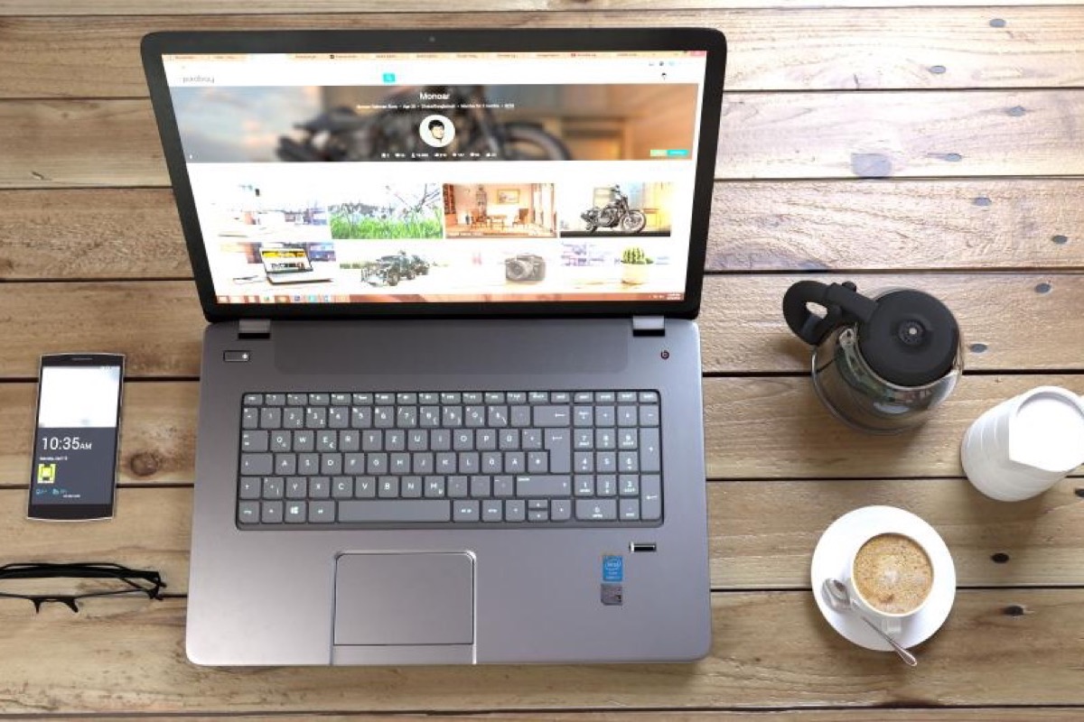 A laptop, a phone and a coffee on a wooden desk.